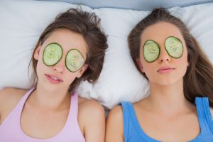 Friends lying in bed with cucumber slices on eyes