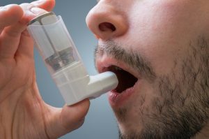 Asthmatic man suffers from asthma and is using inhaler.