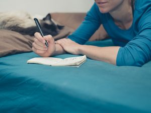 Woman taking notes in bed with cat