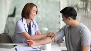 Young Asian female doctor checking blood pressure of male Asian patient