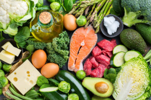 Balanced diet nutrition keto concept. Assortment of healthy ketogenic low carb food ingredients for cooking on a kitchen table. Green vegetables, meat, salmon, cheese, eggs. Top view background