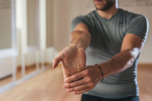 Sporty man stretching forearm before gym workout. Fitness strong male athlete standing indoor warming up.