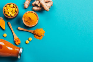 Mess of turmeric plant in different conditions: fresh, dry root, pills, powder and cut plant on blue background. Flat lay style. Place for text.