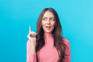 Young beautiful woman having good idea with her finger pointing up isolated on blue background. Success, idea and innovation concept.