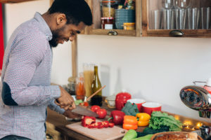 African-american man preparing delicious and healthy food in kitchen, cutting fresh vegetables, copy space