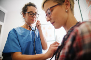 Female middle-aged doctor using stethoscope to examine patient.