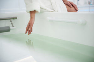 Health treatment concept. Close up portrait of young woman touching water in bath tub before water spa procedure