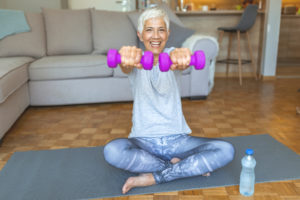 Portrait of mature fitness woman lifting dumbbells. Portrait of happy senior woman holding dumbbell at home. Active senior woman exercising with dumbbell at home