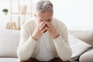 Senior man suffering from headache, sitting on sofa at home