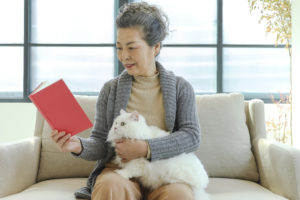 Senior lady, Adult, Pets, Clothing, Embracing, Holding a cat and reading a book.