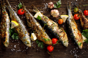 Fried fishes with addition of herbs, spices and lemon slices on a wooden background. Seafood, sardines
