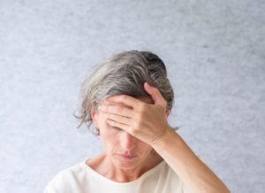 Closeup of middle aged woman looking down with hand over forehead against grey background (selective focus)