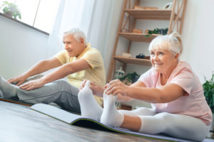Senior man and woman doing yoga together indoors holding feet legs stretching smiling