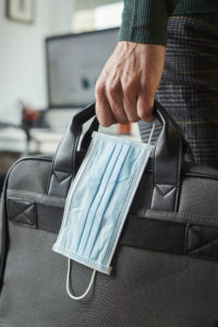 closeup of a young man in an office holding a briefcase and a surgical mask in his hand