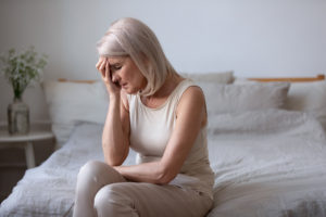 Seated in bed in the morning middle-aged woman touch face with hand closed eyes suffers from barometric pressure headache migraine, old female feels unhappy upset health or personal problems concept