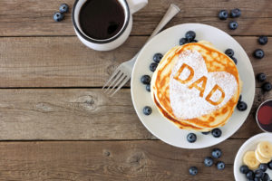 Pancakes with heart shape and DAD letters. Fathers Day breakfast concept. Above view corner border on a rustic wood background.