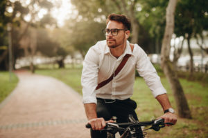 Man enjoying music using earphones while commuting to office on a bicycle. Businessman biking to office while listening to music.
