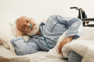 Older sick man with a oxygen mask lying in a hospital bed