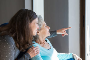 Adult daughter visiting elderly mother. Young woman showing to senior lady scene out of window. Dementia concept