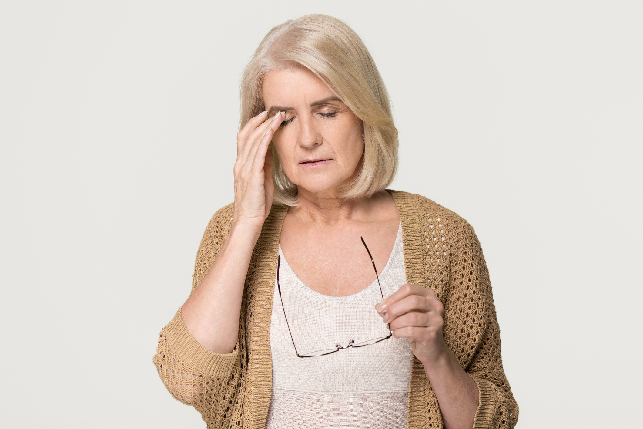 Upset tired old mature woman taking off glasses feeling eyestrain pain, stressed aged senior lady suffer from headache bad vision eye strain fatigue problem isolated on grey white studio background