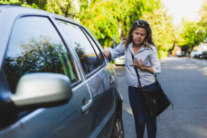 Weak young woman having chest pain while leaning against a car outdoors - Casually dressed female worker feeling tired while having breathing and respiratory problems on the street