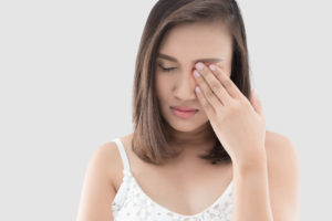 Asian woman suffering from strong eye pain against gray background. Female has a pain in the eye. Healthcare concept. Having migraine