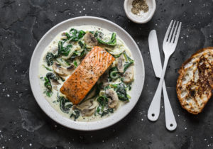 Baked salmon with creamy spinach mushrooms sauce on a dark background, top view. Salmon florentine
