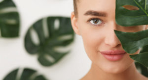 Woman with natural make up and green leaf over background, covering half of face