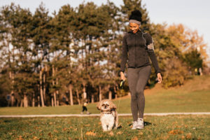 Happy black athletic woman walking with her dog in the park.