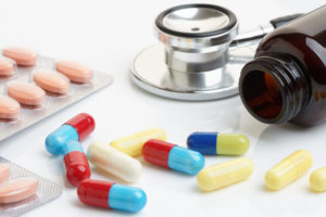 Close up of statin and beta-blocker pills and capsules with bottle and stethoscope.
