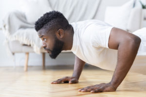 Young black man exercising in his house gym, doing push ups, side view, free space