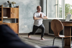 Senior hispanic man standing in warrior yoga pose variation practicing in living room alone