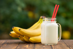 banana smoothie in mason jar on wooden table with green blurred natural background