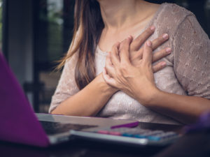 Closeup woman having heart attack. Woman touching breast and having chest pain after long hours work on computer. Office syndrome concept.