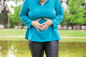 Woman suffering from belly ache. Plus sized lady standing in park and touching stomach. Health problem concept