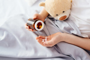 Child taking medicines pills. Sick eight years boy lying in bed