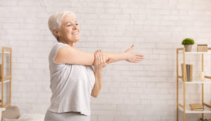 Morning work-out. Positive senior lady warming up her hands at home, empty space