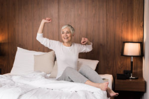 Cheerful senior woman with big beautiful smile waking up and stretching in her bedroom, Joy of the new day concept