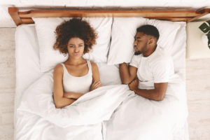 Divorce and separation. Millennial african couple in bed having problems, wife angry, husband sleeping, top view