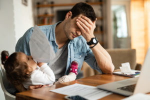 Young father feeling exhausted and having a headache while babysitting his small daughter and working at home.