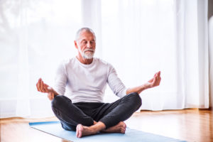 Active senior man meditating at home, eyes closed.