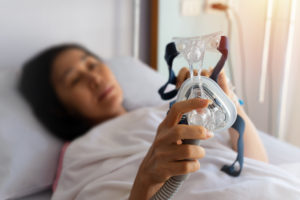 Senior patient woman hands holding Cpap mask lying in hospital room.