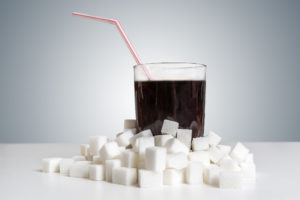 Cola drink in glass and many sugar cubes around. Unhealthy eating concept.