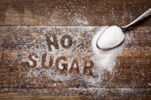 high-angle shot of a wooden table sprinkled with sugar where you can read the text no sugar and a spoon full of sugar