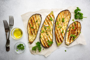 Grilled eggplant slices, garnished with fresh herbs, on white background, top view