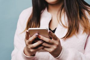 Young Teen Female sends a text with her smart phone with a fashionable coat