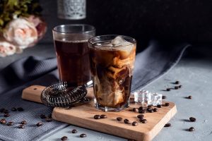 Iced coffee in a tall glass with cream on dark background