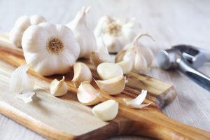 Bulbs of garlic on cutting board and garlic press on light background