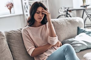 Frustrated young woman suffering from the headache while sitting on the sofa at home