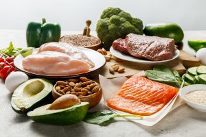 raw salmon, meat and chicken breasts near green vegetables isolated on grey, ketogenic diet menu